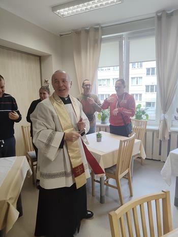 Ksiądz trzymający kropidło na tle modlących się osób